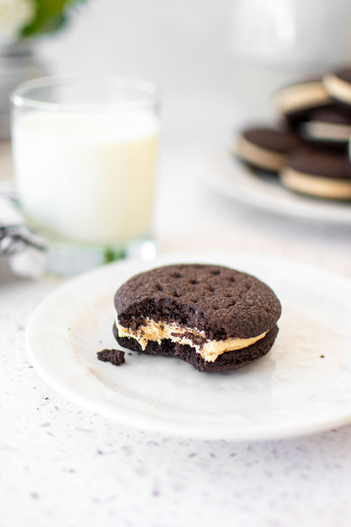homemade peanut butter oreo with a bite taken out on a plate on a white marble counter with a glass of milk.