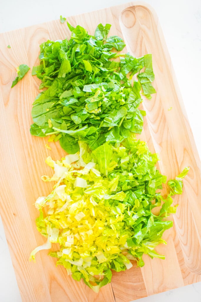 chopped romaine lettuce and spinach on a wood cutting board.