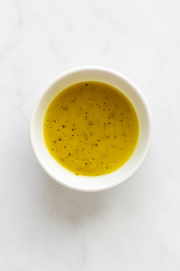 homemade lemon dressing in a bowl on a white marble countertop.