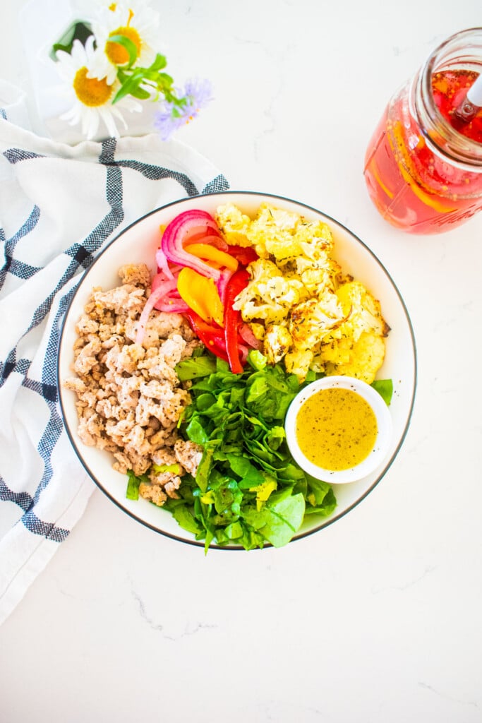 large salad bowl with roasted cauliflower, ground turkey, pickled onions, lettuce and lemon dressing on a marble counter.