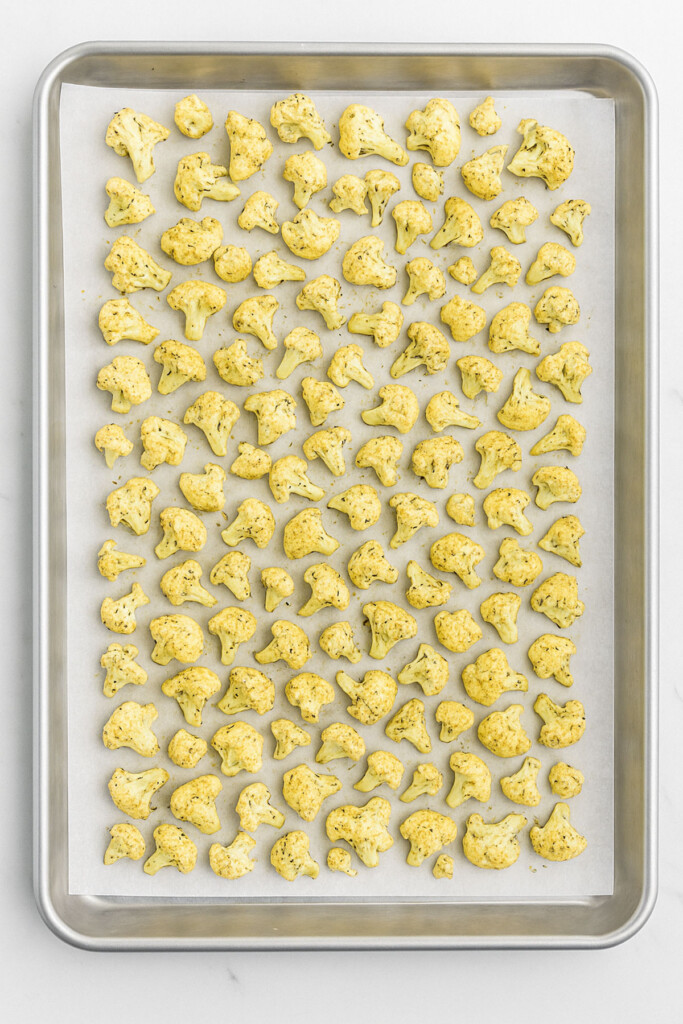 seasoned cauliflower on a baking sheet on a white marble countertop.