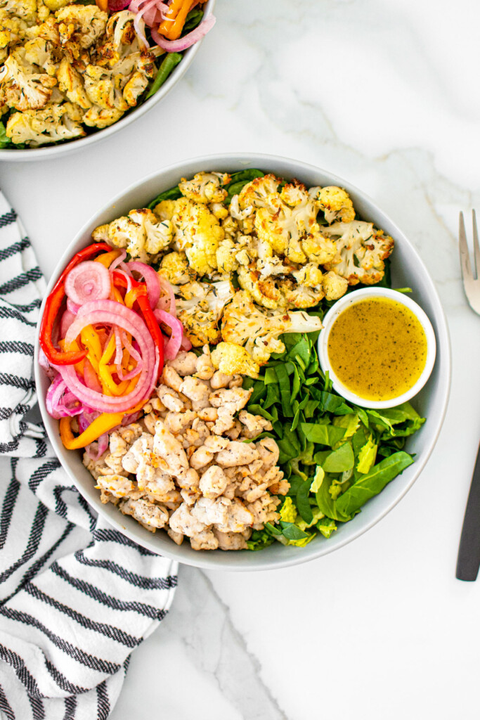roasted cauliflower turkey salad with lemon dressing in a bowl on a white marble countertop.