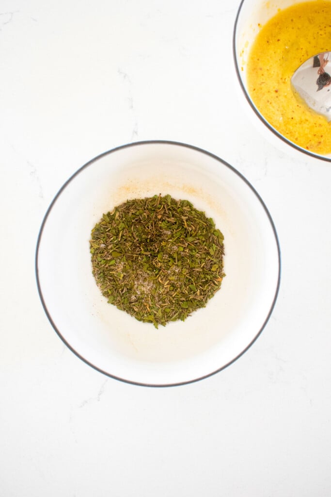 herbs mixed together in a small bowl on a white marble counter.