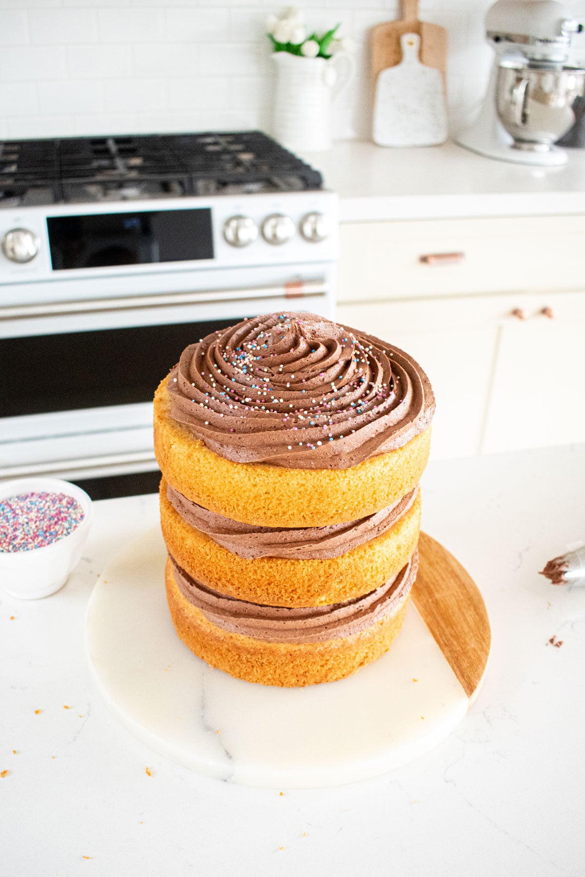 simple naked birthday cake being assembled on a white marble counter.