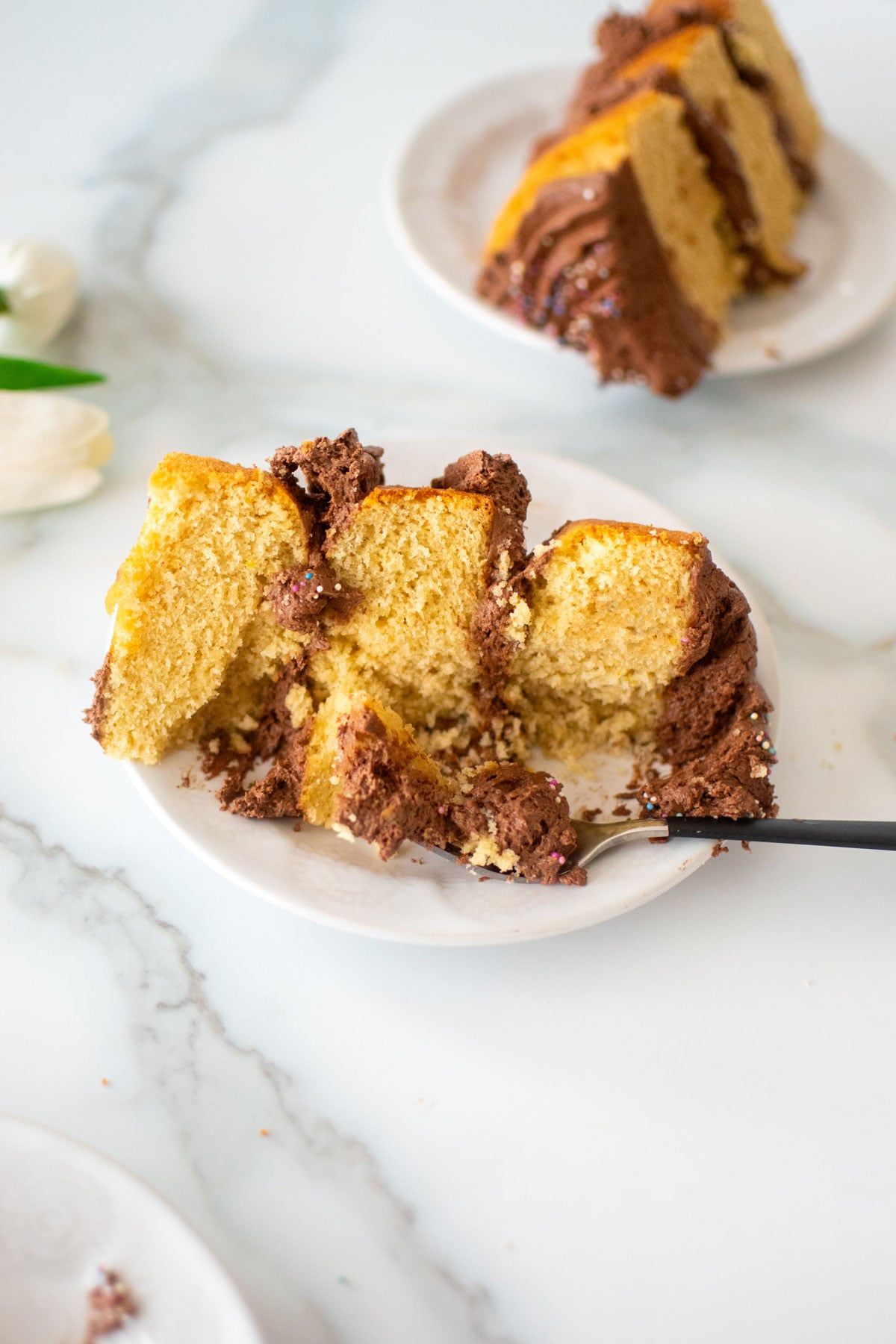 slice of simple naked birthday cake on a cake plate on a white marble counter.