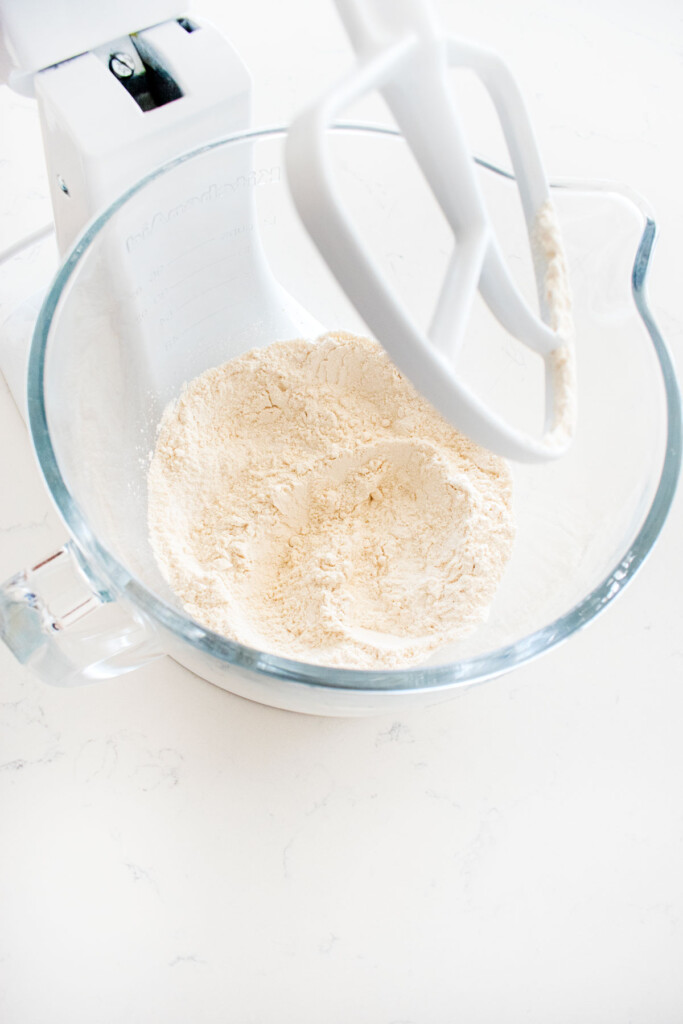 flour, baking soda and salt in a glass stand mixing bowl on a white marble counter.