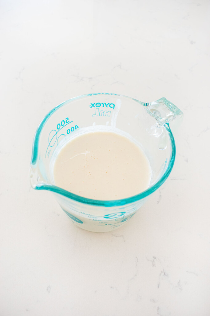 buttermilk mixed with sourdough discard in a liquid measuring cup on a white marble counter.