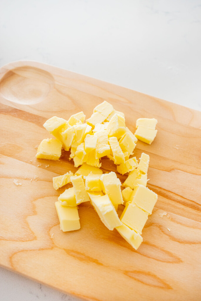 butter chopped into cubes on a wood cutting board on a white marble counter.