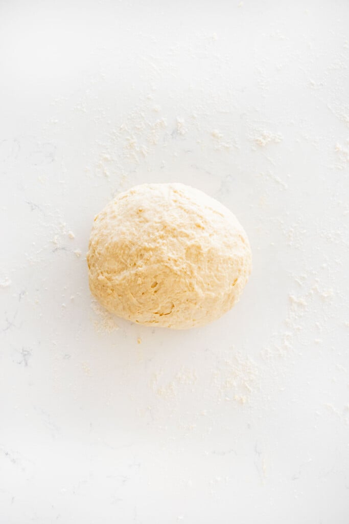 sourdough irish soda bread dough formed into a ball on a white marble counter.