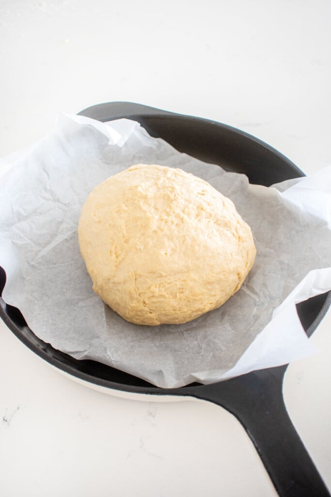 sourdough irish soda bread dough ball in a cast iron skillet on a white marble counter.