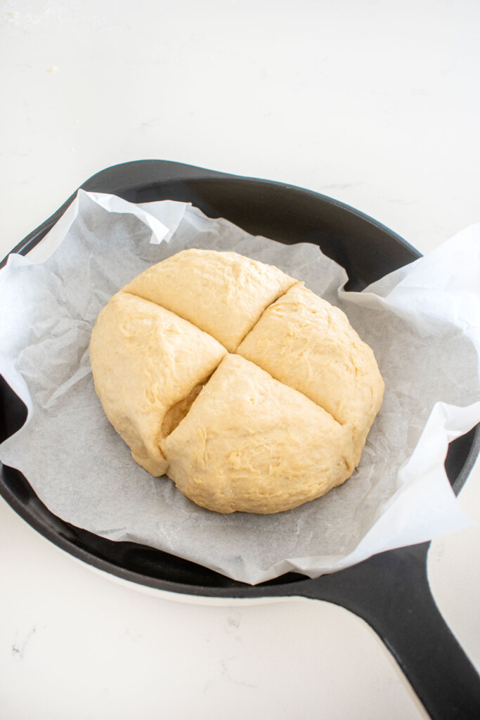 sourdough irish soda bread dough ball sliced into four quarters in a cast iron skillet on a white marble counter.