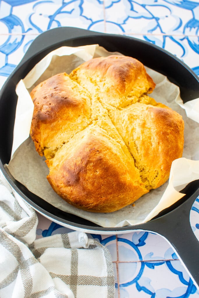 sourdough irish soda bread in a cast iron skillet on a blue tile table.