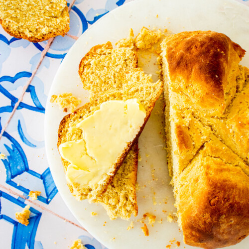 sourdough irish soda bread sliced with a pat of butter on one of the slices on a marble serving board on a blue tile table.