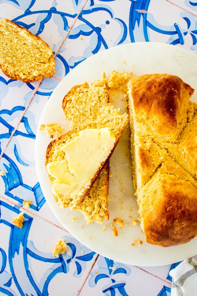 sourdough irish soda bread sliced with a pat of butter on one of the slices on a marble serving board on a blue tile table.