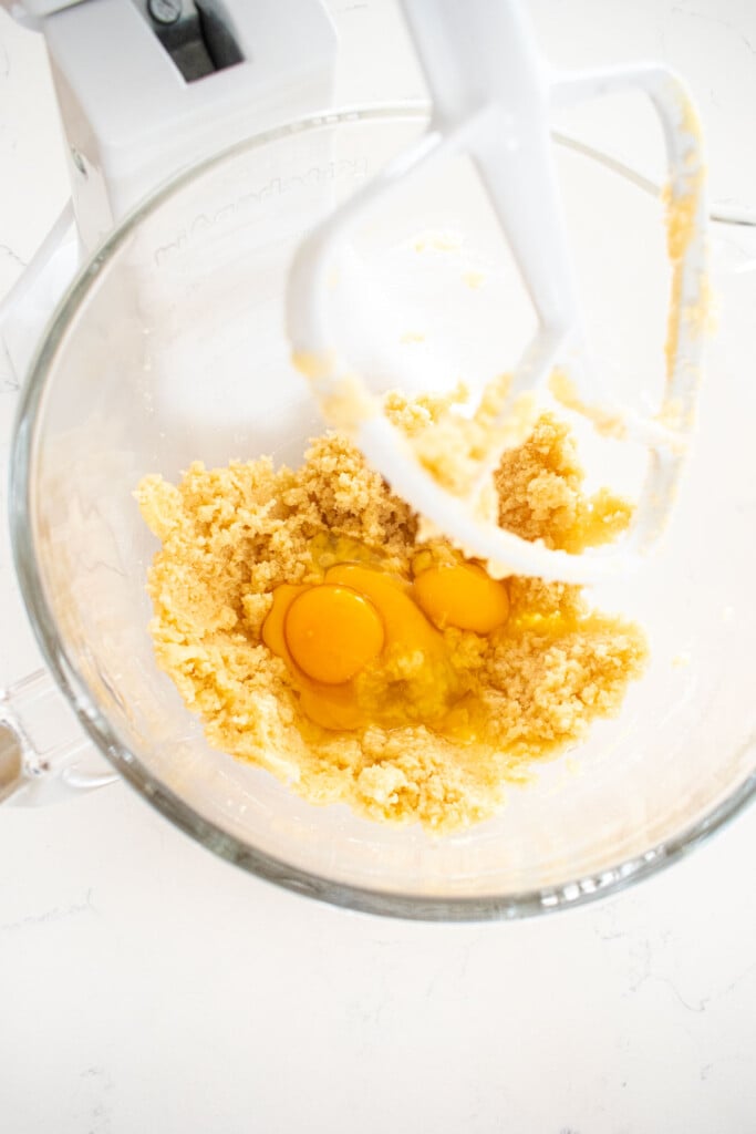 creamed butter and sugar with eggs in a glass mixing bowl on a white marble counter.
