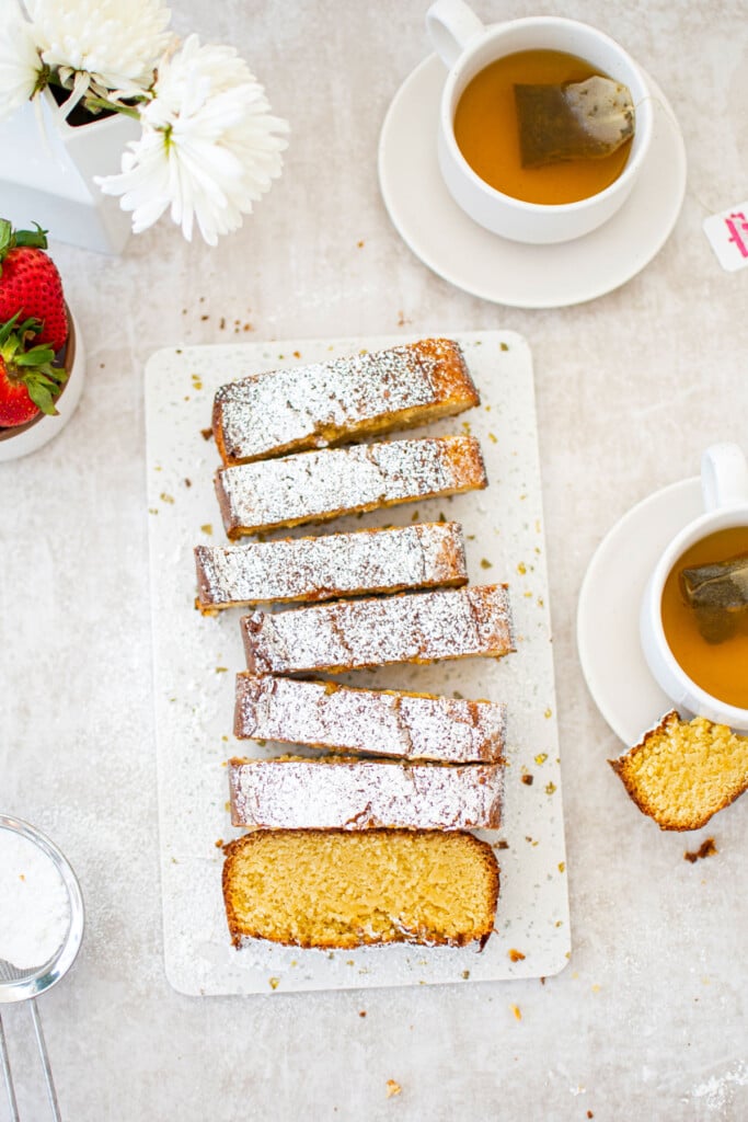 traditional butter pound cake loaf sliced on a marble cutting board with tea cups and fresh strawberries.