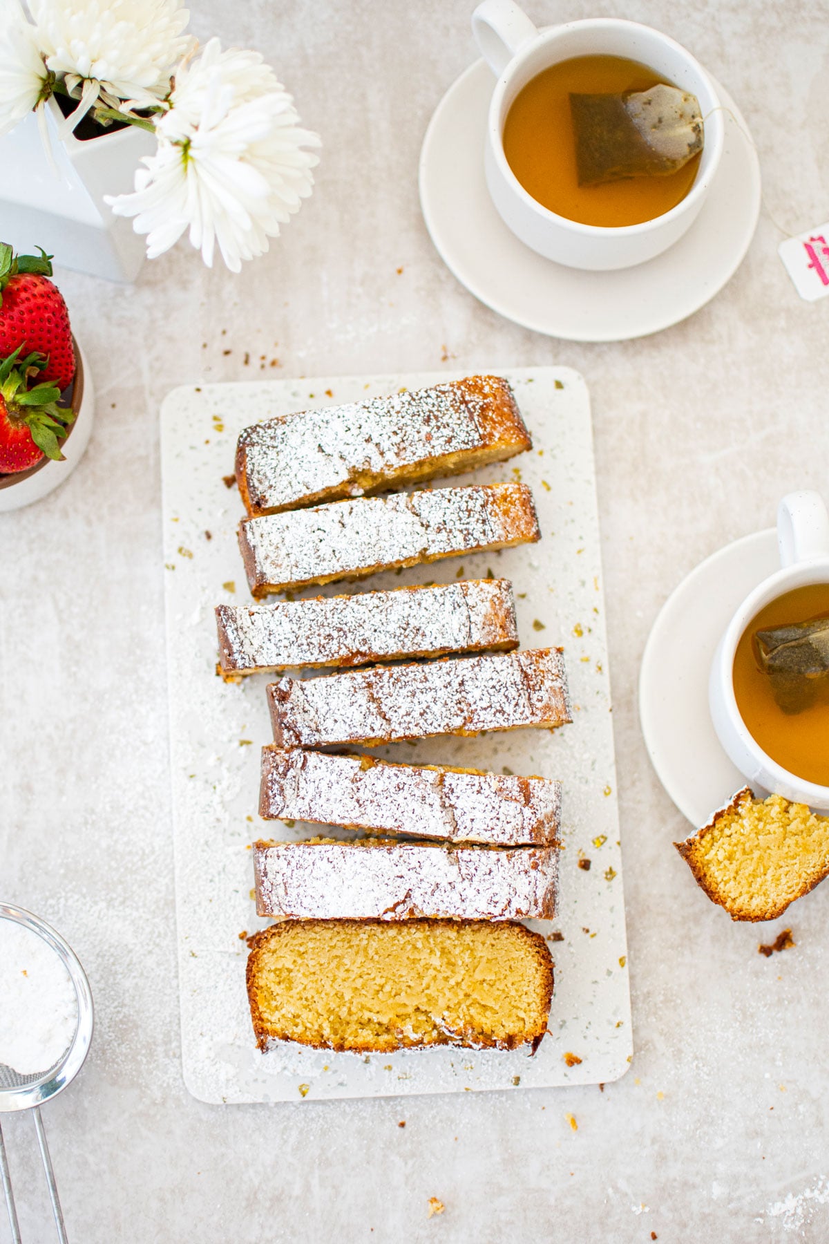 traditional butter pound cake loaf sliced on a marble cutting board with tea cups and fresh strawberries.