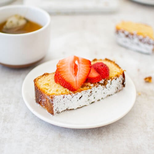 slice of traditional butter pound cake loaf on a white plate with fresh strawberries on top.