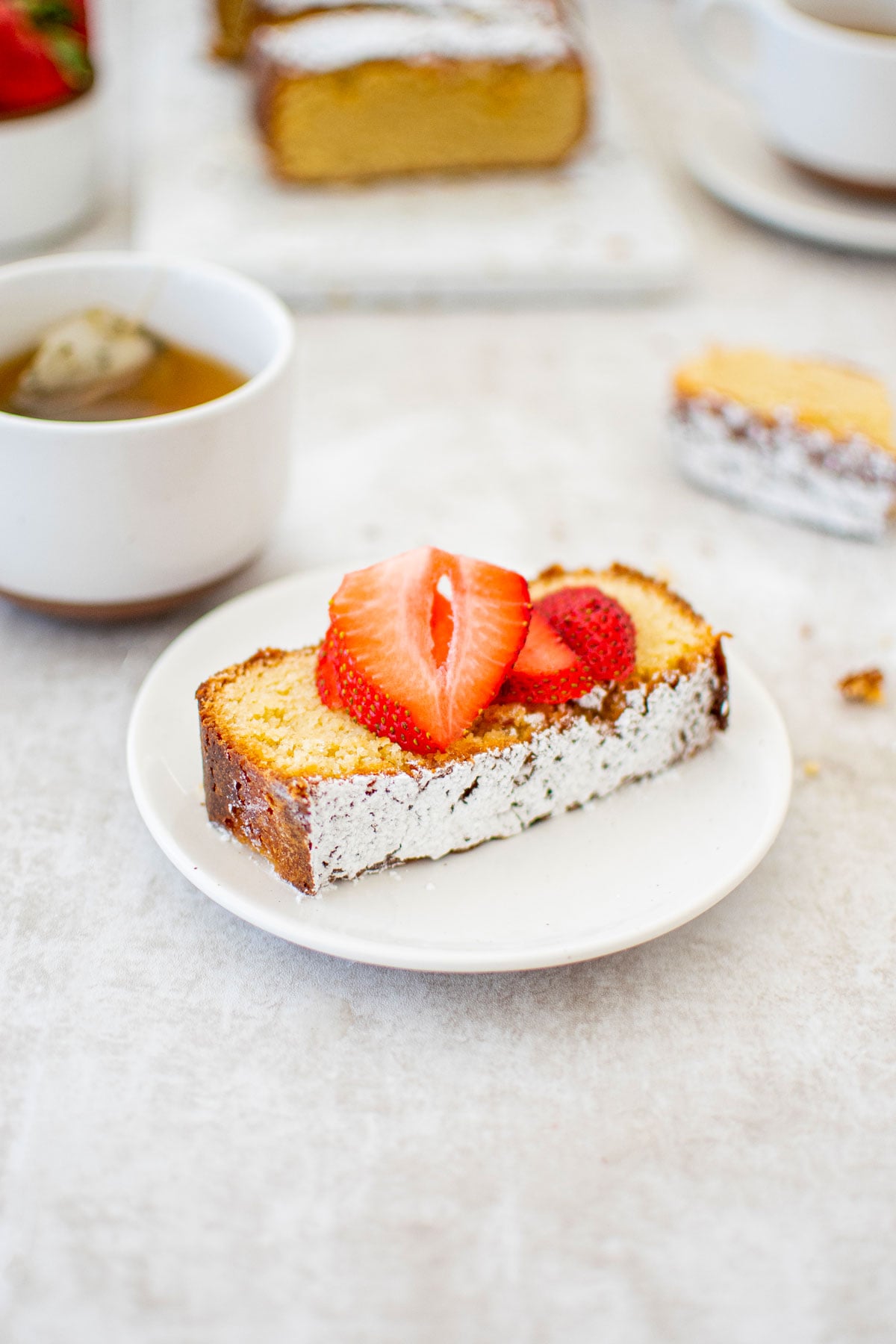 slice of traditional butter pound cake loaf on a white plate with fresh strawberries on top.