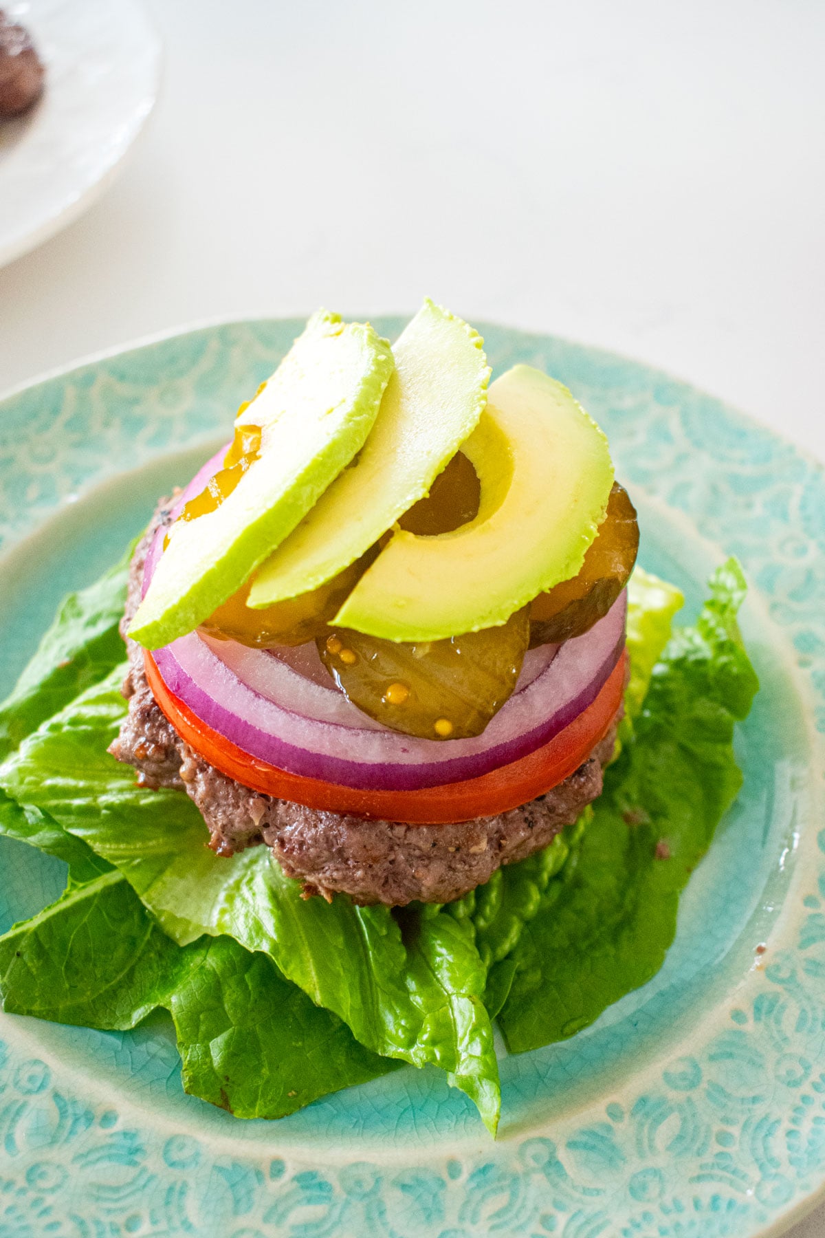 avocado lettuce wrap burger being assembled on a plate on a marble counter.