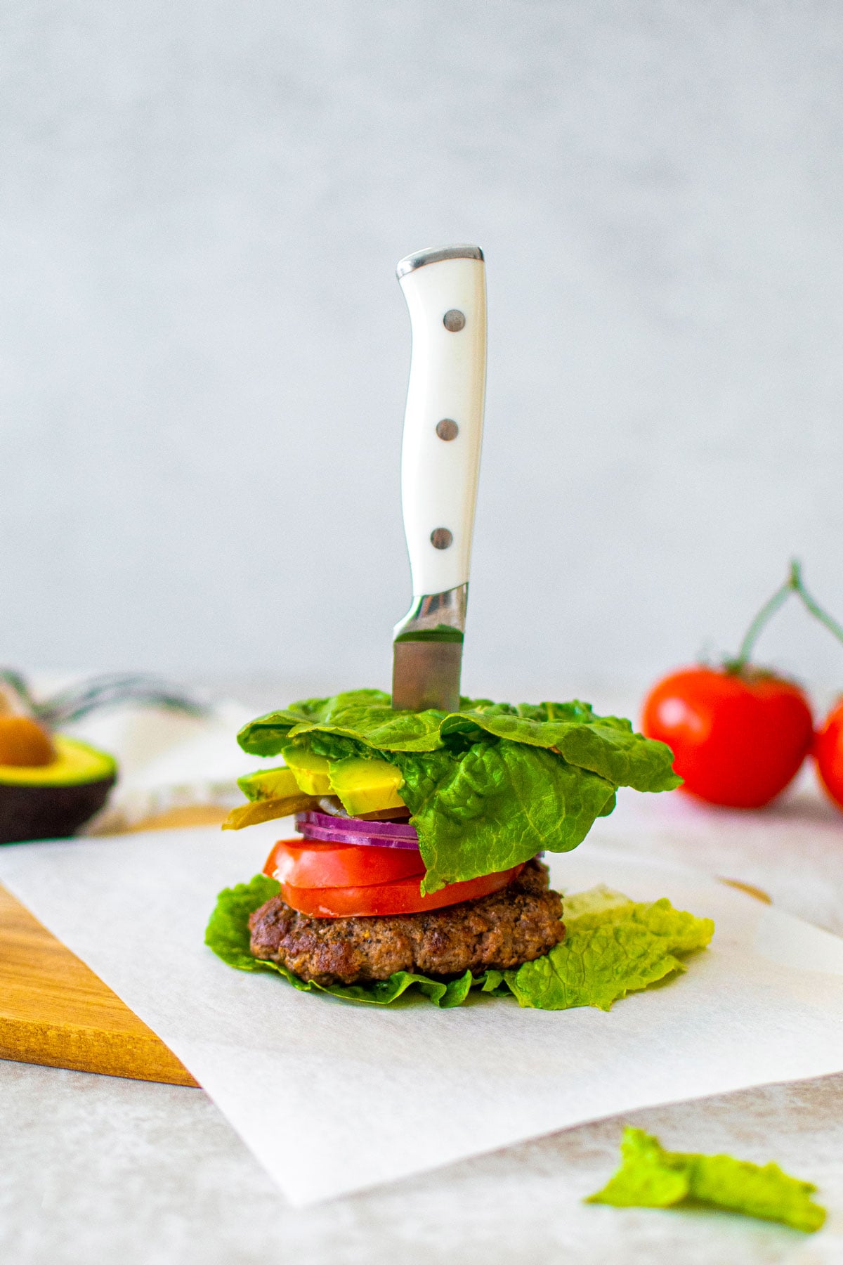 avocado burger lettuce wrap being assembled with a knife in it on a wood cutting board.