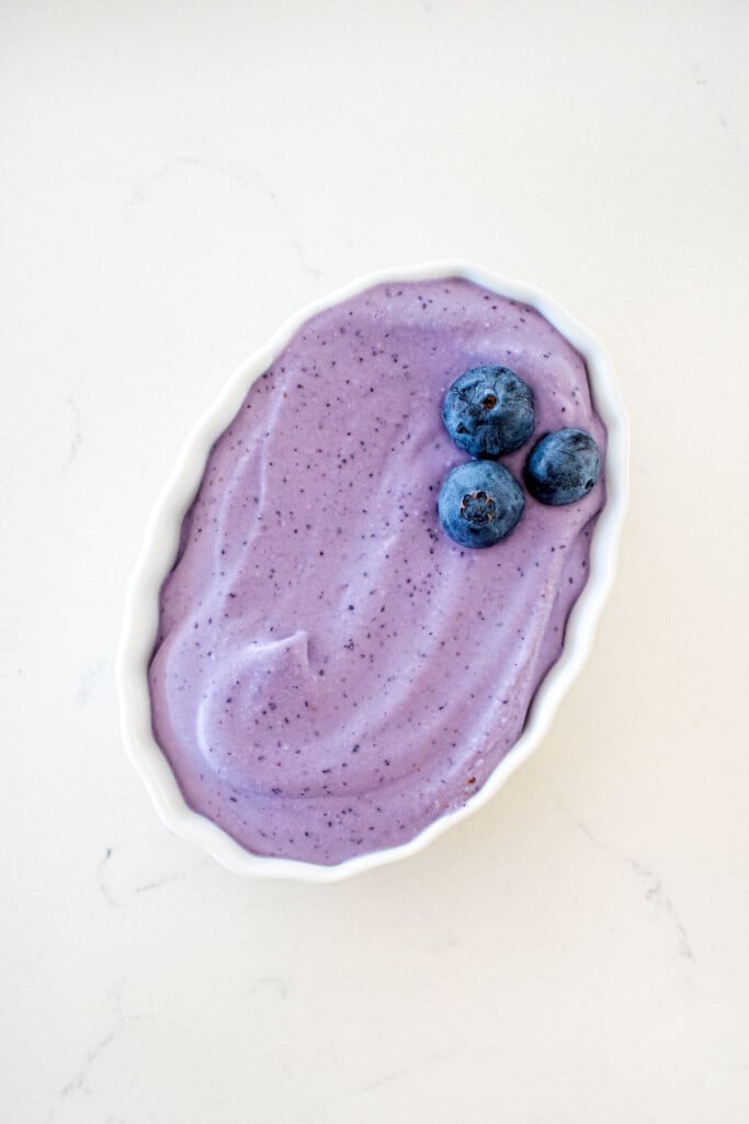 homemade blueberry pup cup in a small dish with fresh blueberries on a white marble counter.