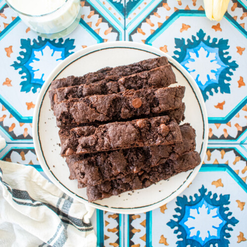 simple chocolate espresso biscotti piled onto a plate on a tile table with a glass of milk and fresh tulips.