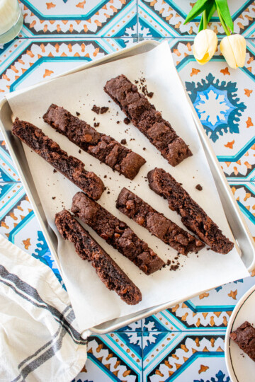 simple chocolate espresso biscotti on a baking sheet on a tile table with fresh tulips.