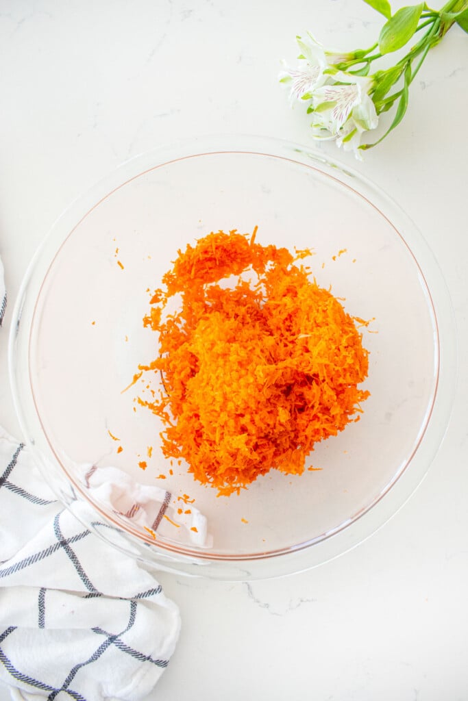 glass mixing bowl on a white marble counter with finely grated carrots.