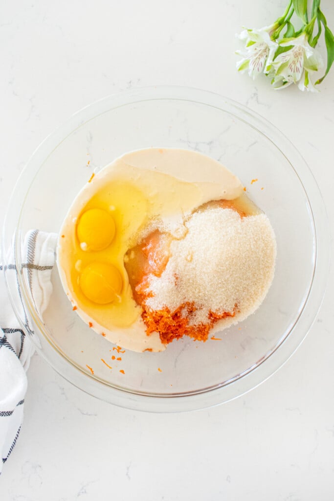 wet ingredients for sourdough carrot snack cake in a glass mixing bowl on a white marble counter.