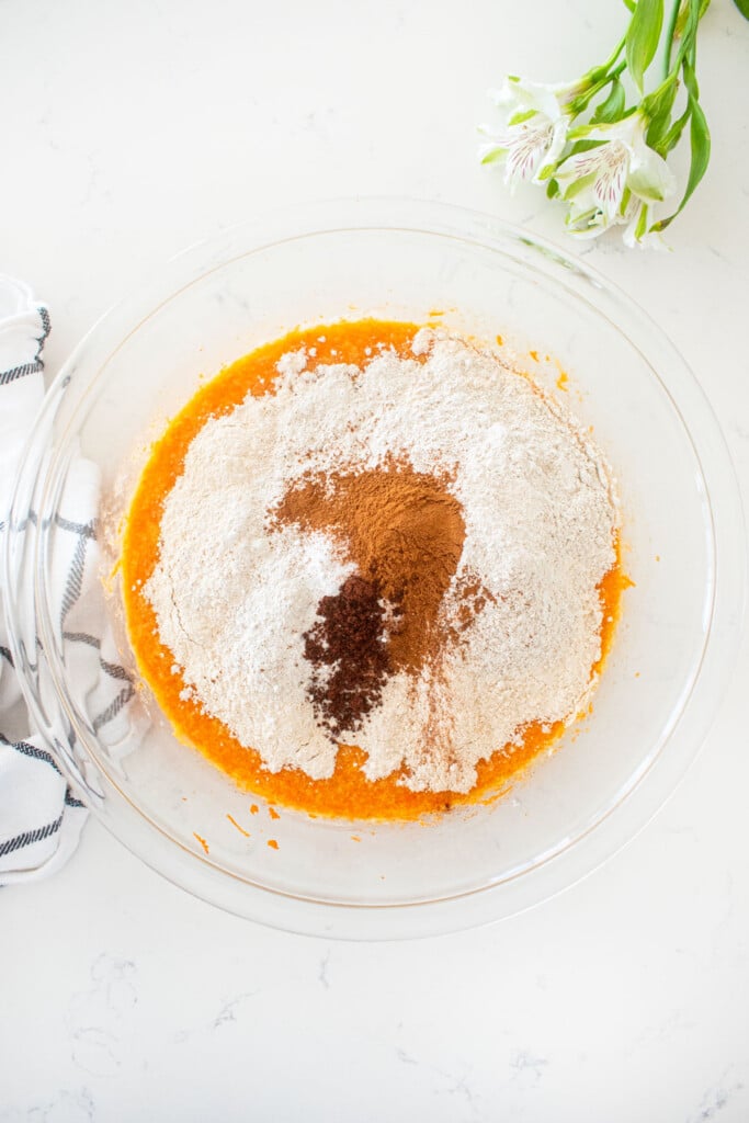 dry ingredients on top of wet ingredients for sourdough carrot snack cake in a glass mixing bowl on a white marble counter.