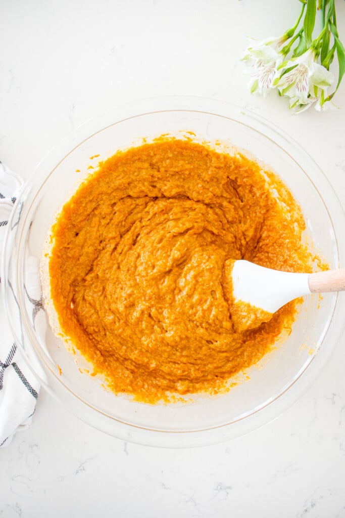 sourdough carrot snack cake batter in a glass mixing bowl with a spatula on a white marble counter.