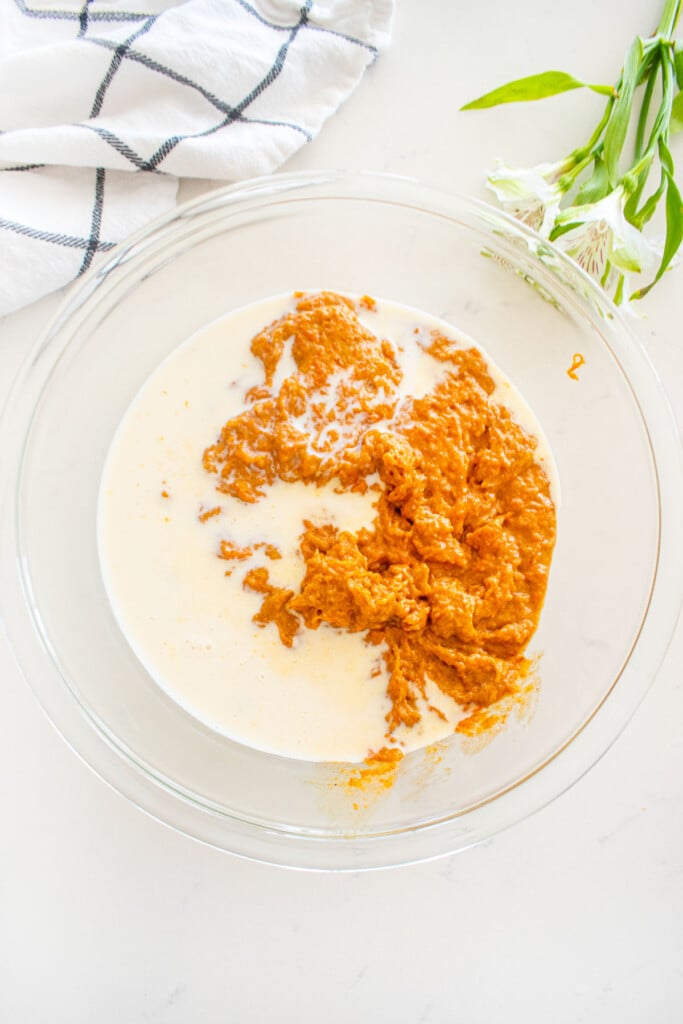 sourdough carrot snack cake batter with coffee creamer in a glass mixing bowl on a white marble counter.