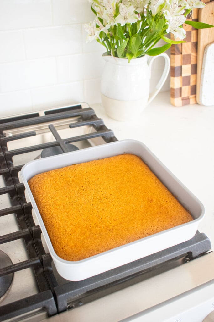 baked carrot snack cake in a square pan cooling on top of an oven.