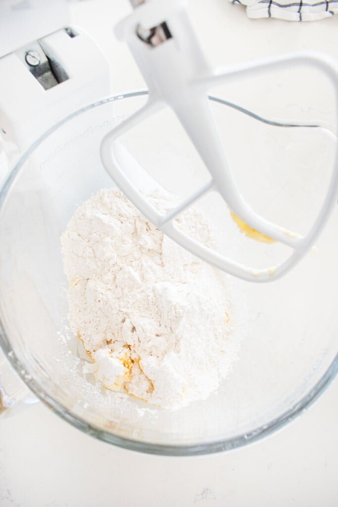 ingredients for cream cheese frosting in a glass stand mixing bowl on a white marble counter.