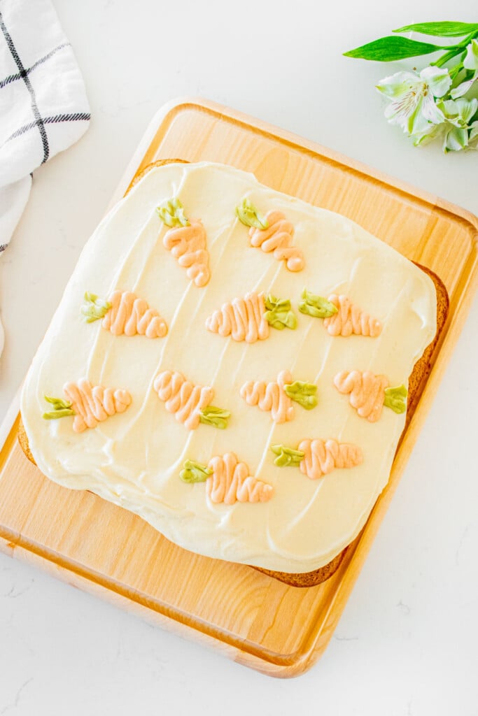 sourdough carrot snack cake on a wood serving board with cream cheese frosting spread on top with piped carrots on a marble counter.