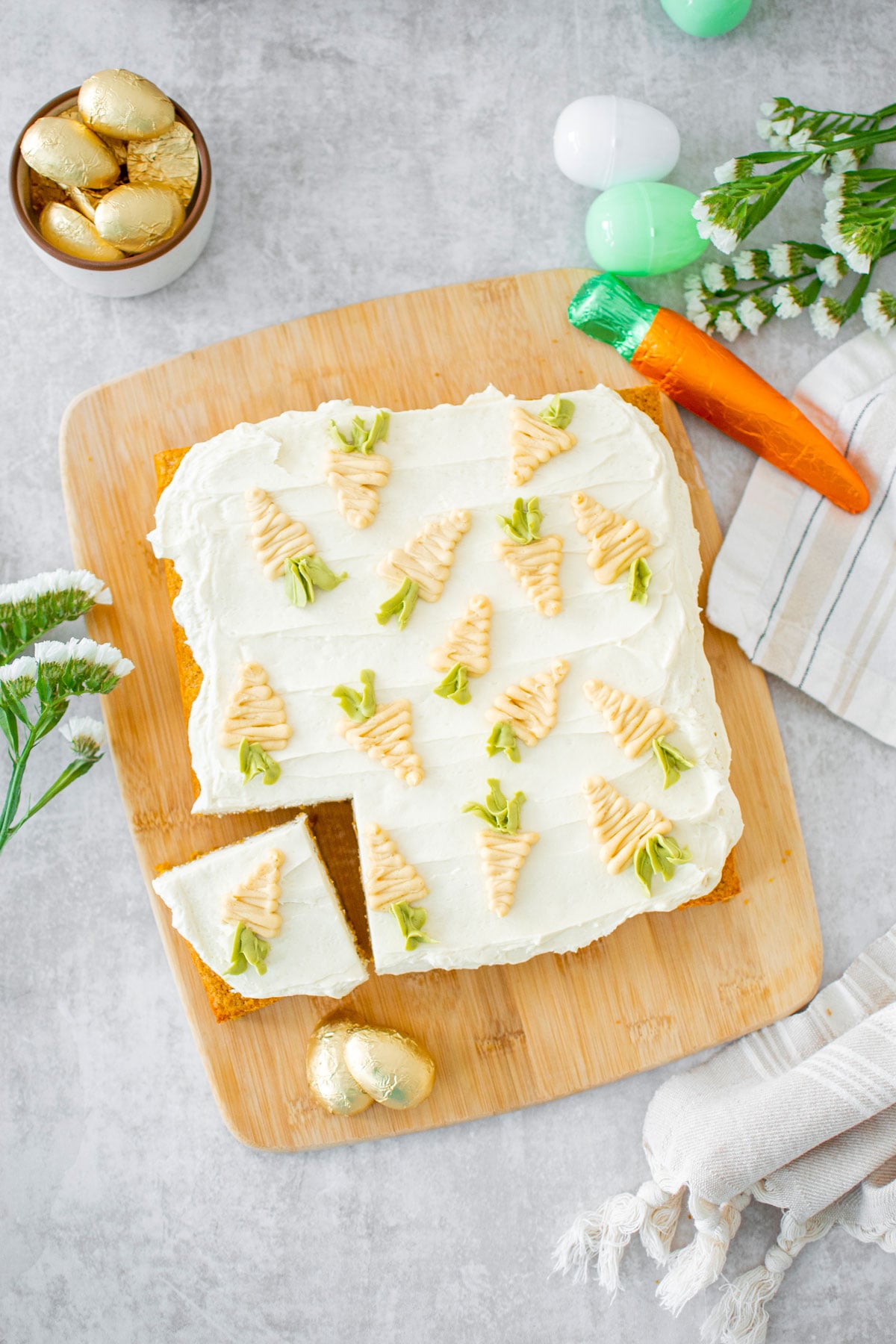 sourdough carrot snack cake with piped buttercream carrots on top cut into a square slice on a wood cutting board.