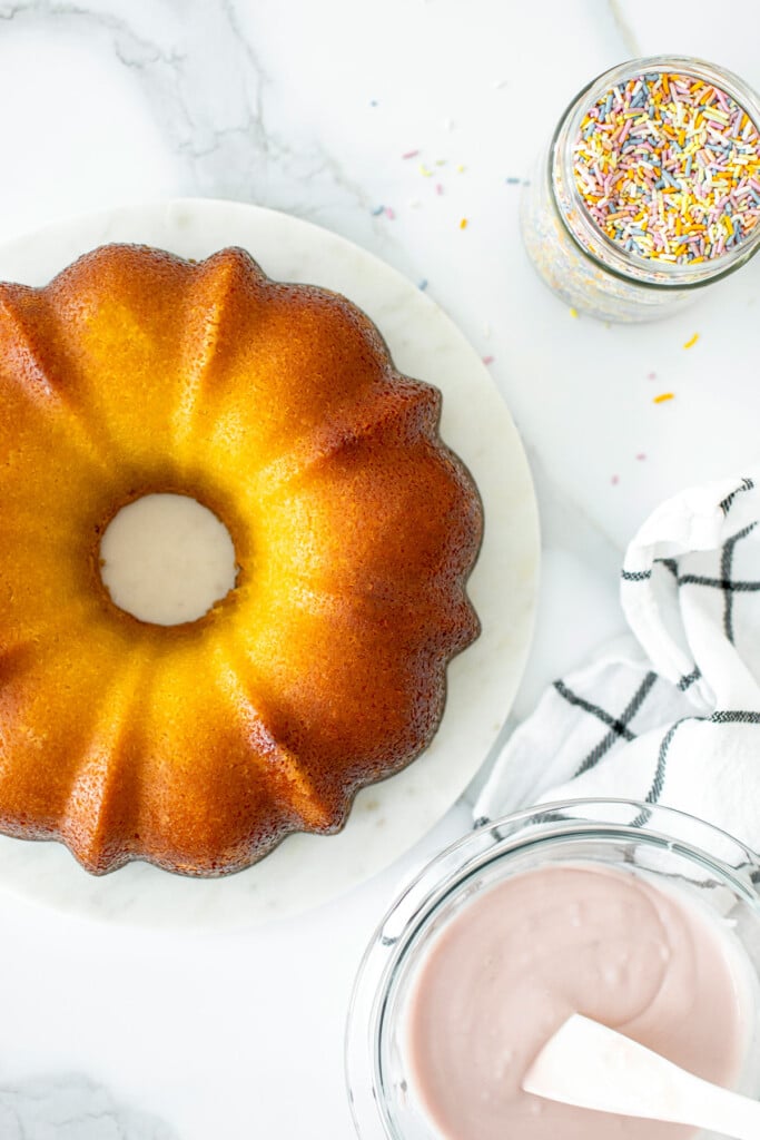 strawberry donut pound cake on a white marble counter with pink frosting and sprinkles on the side.