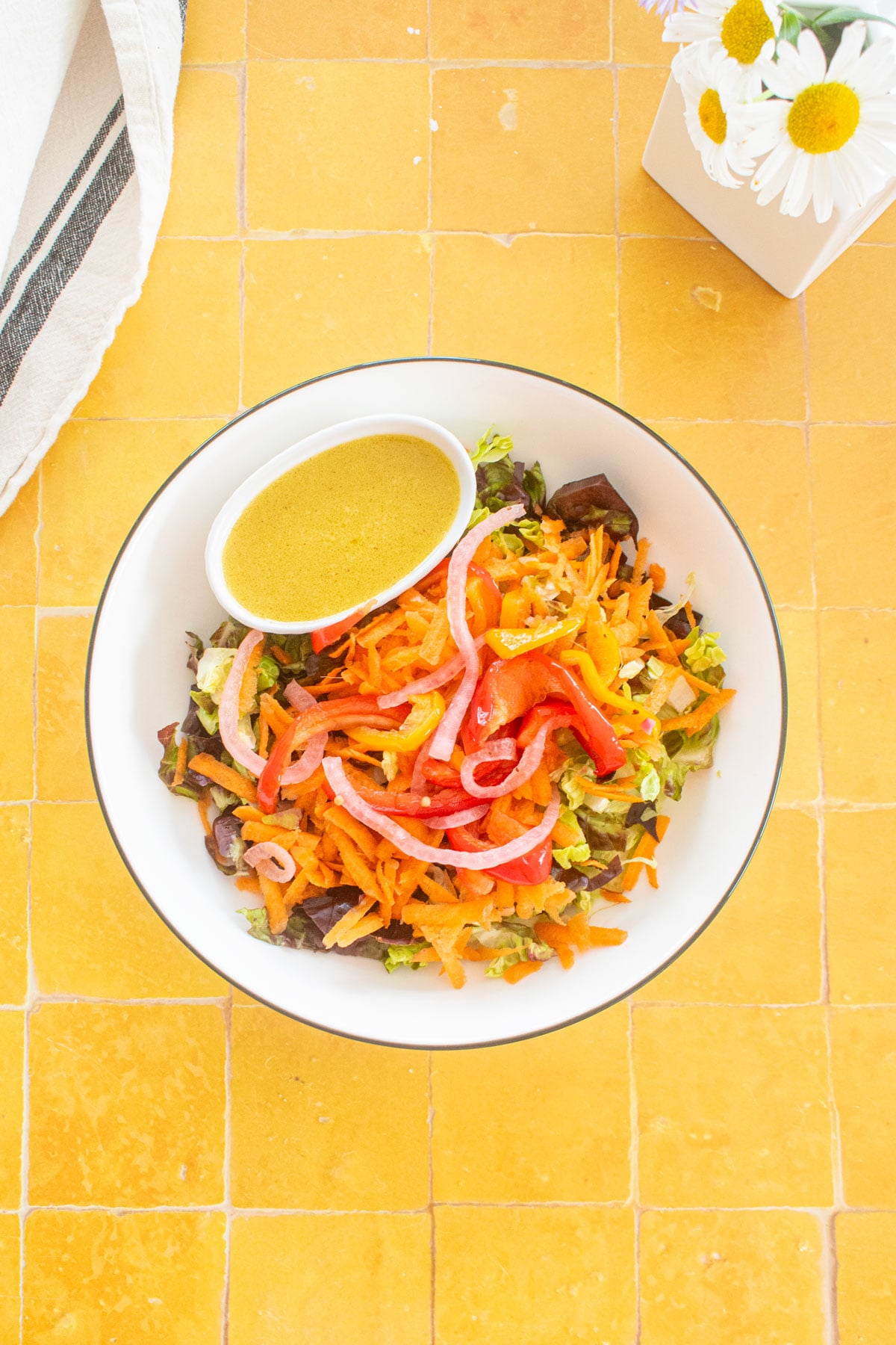 salad bowl with a small dish of honey mustard dressing in a small dish on a yellow tile table with fresh flowers.