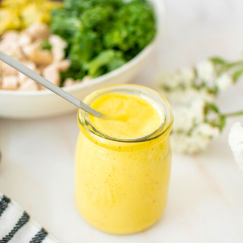 vegan honey mustard dressing in a small glass jar on a marble counter with a salad in the background.