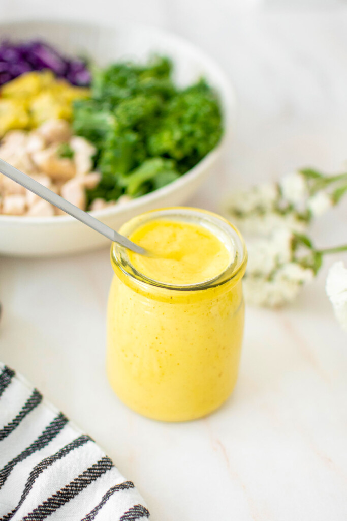vegan honey mustard dressing in a small glass jar on a marble counter with a salad in the background.