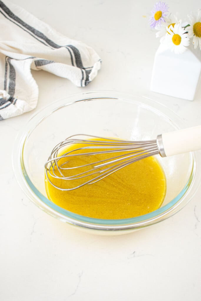 glass bowl with vegan honey mustard dressing and a whisk on a marble counter.