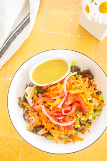 salad bowl with a small dish of honey mustard dressing in a small dish on a yellow tile table with fresh flowers.