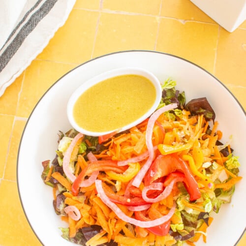 salad bowl with a small dish of honey mustard dressing in a small dish on a yellow tile table with fresh flowers.