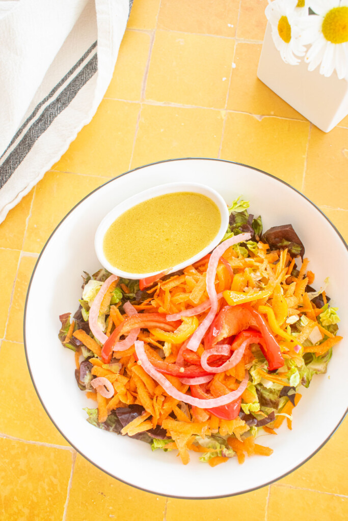 salad bowl with a small dish of honey mustard dressing in a small dish on a yellow tile table with fresh flowers.