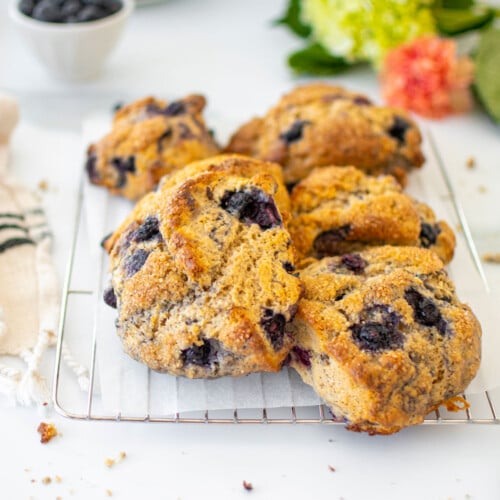 blueberry cream cheese scones on a cooling rack on a white marble counter with a bowl of blueberries.