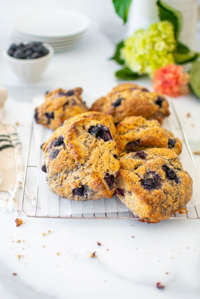 blueberry cream cheese scones on a cooling rack on a white marble counter with a bowl of blueberries.