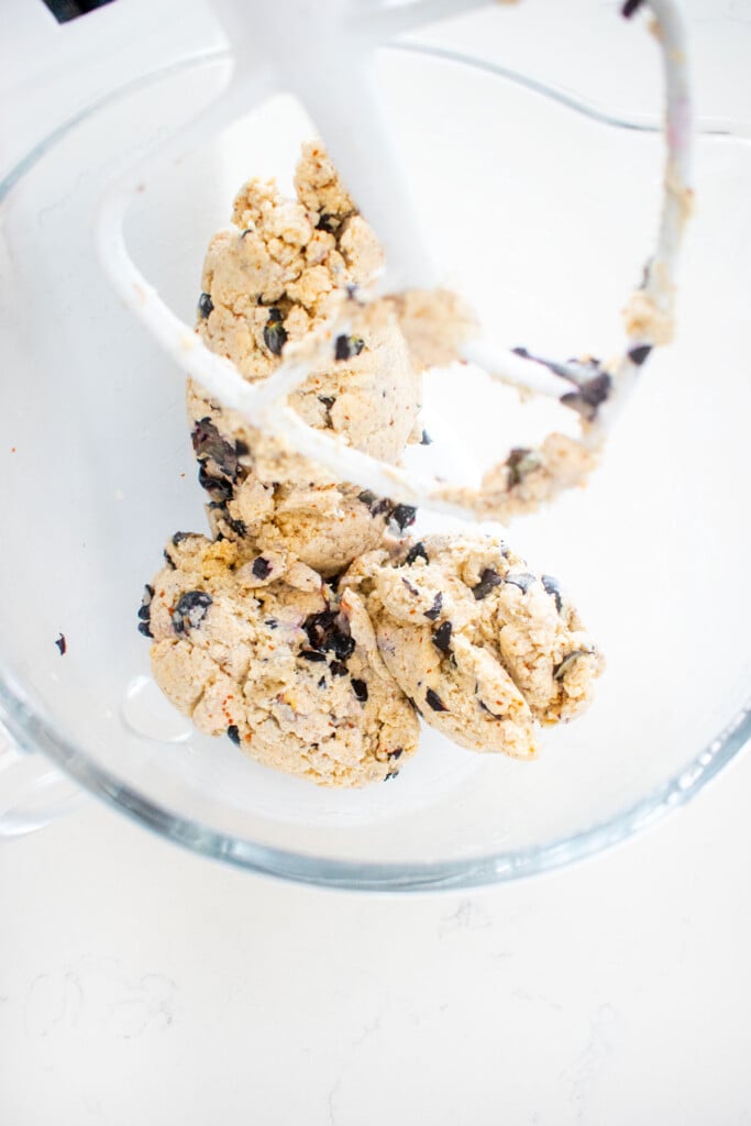 blueberry cream cheese scones dough in a glass stand mixing bowl on a white marble counter.