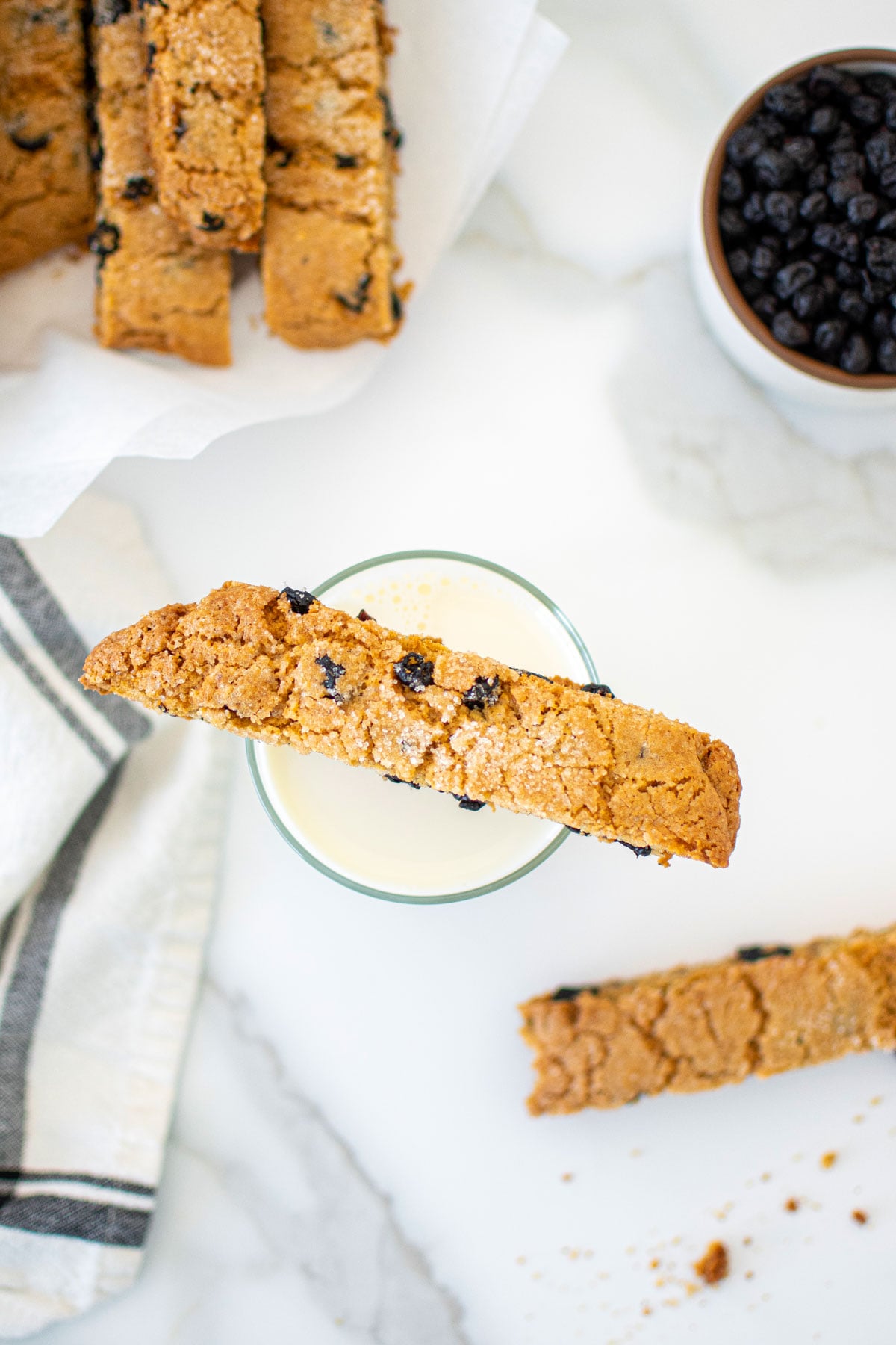 blueberry muffin biscotti sitting on top of a glass of milk on a marble counter.
