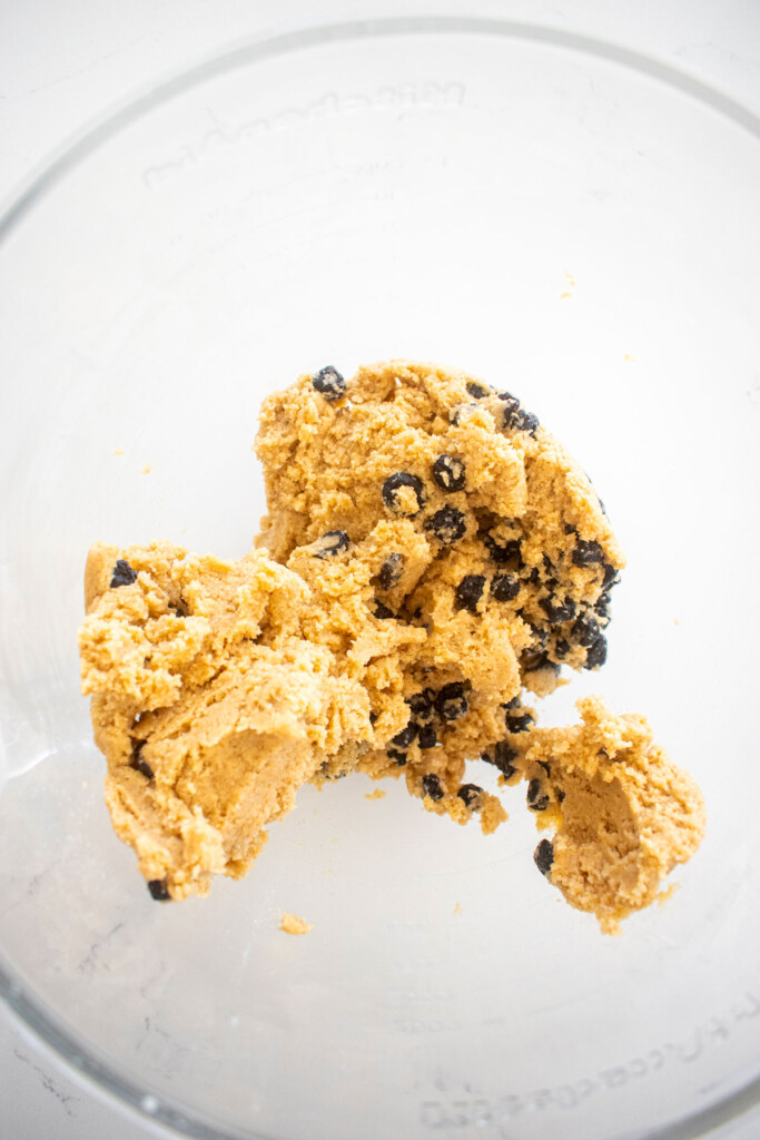 blueberry muffin biscotti cookie dough in a glass mixing bowl on a white marble counter.